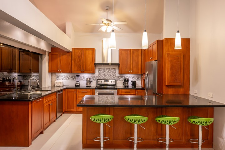 Modern kitchen with wood cabinets, stainless steel appliances, and green bar stools at a black countertop island.