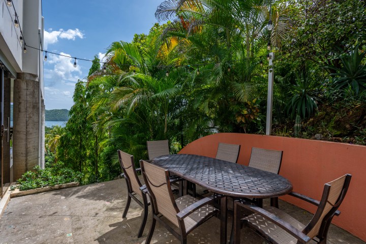Outdoor patio with table and chairs, surrounded by lush greenery and string lights.