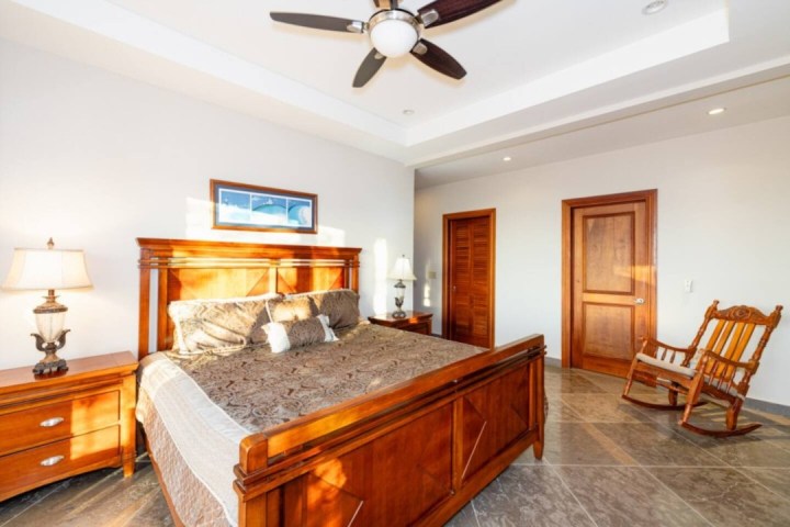 Bedroom with wooden furniture, including bed and rocking chair, ceiling fan, lamps, and brown doors.