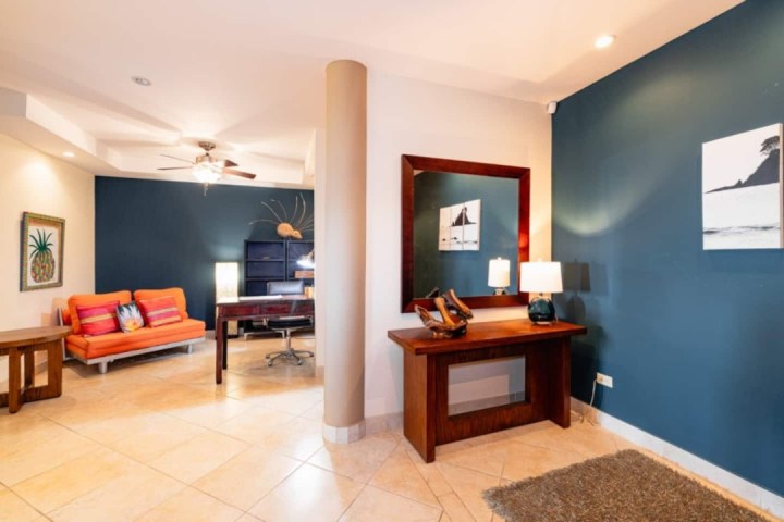 Spacious room with orange couch, desk, large mirror, and blue accent wall.