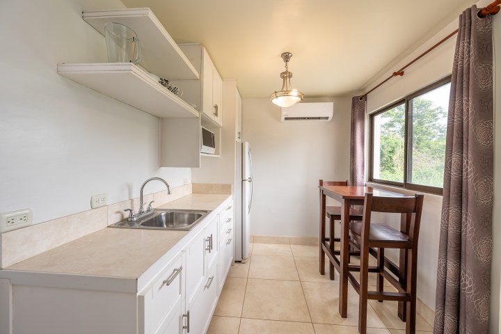 Small kitchen with white cabinets, sink, and a table with two chairs by a window.