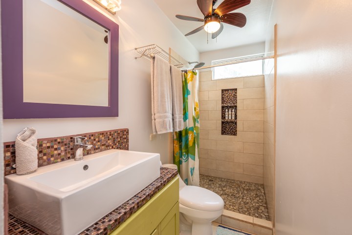 Bathroom with sink, purple mirror, shower with patterned curtain, and a ceiling fan with light.