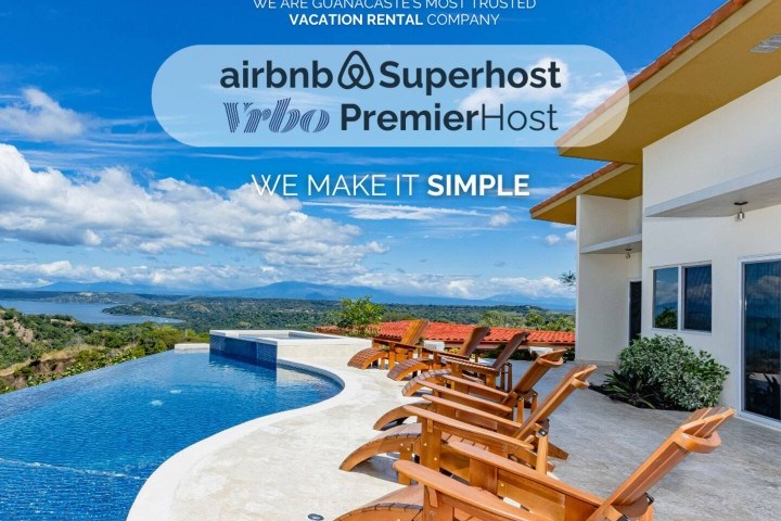 Outdoor pool area with deck chairs overlooking scenic landscape, featuring vacation rental company logos.