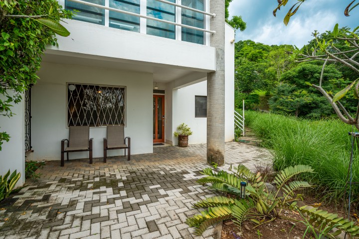 Outdoor patio with two chairs, potted plant, and surrounding greenery beside a modern building.