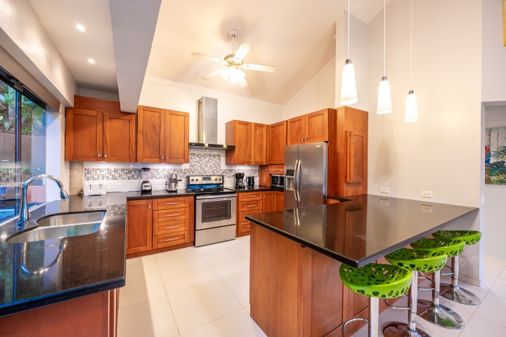 Modern kitchen with wooden cabinets, black countertops, stainless steel appliances, and green stools.