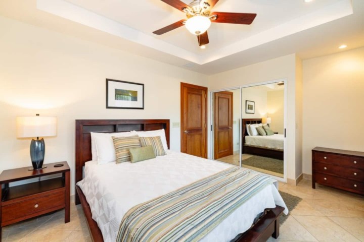 Bedroom with wooden bed, two nightstands, mirror closet doors, ceiling fan, and framed artwork.