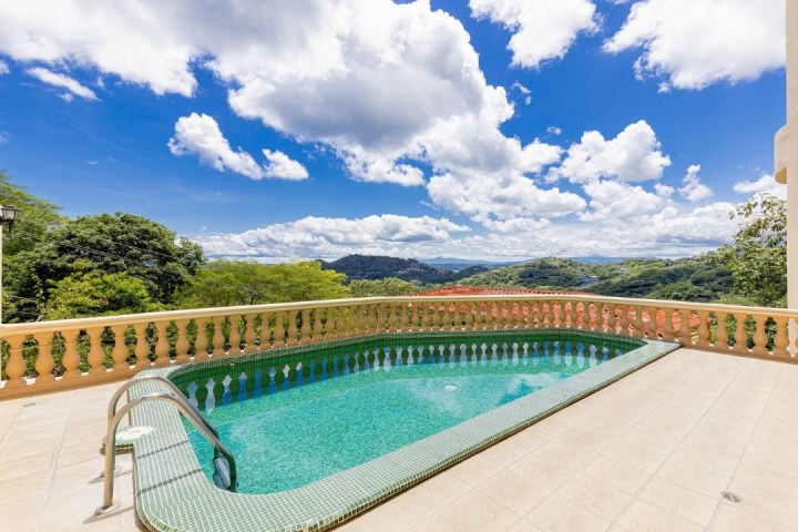 Terrace with pool overlooking hills under a blue sky with clouds.