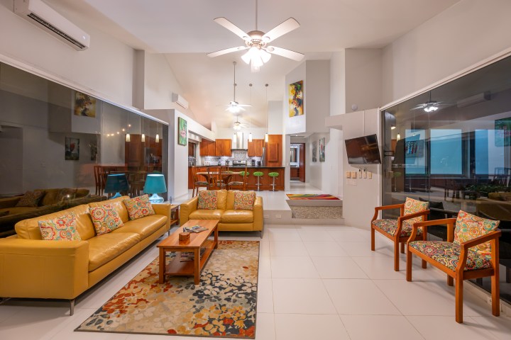 Modern living room with yellow sofa, patterned chairs, and open kitchen view.