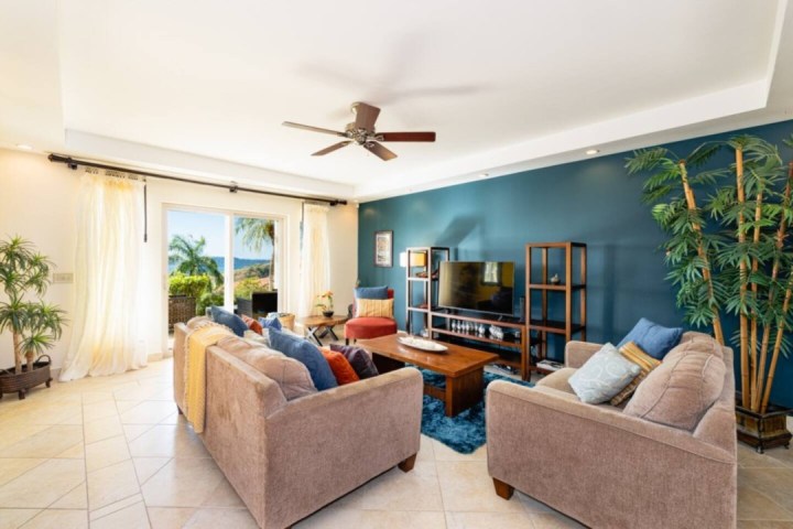 Bright living room with sofas, TV, and large window showing outdoor greenery.