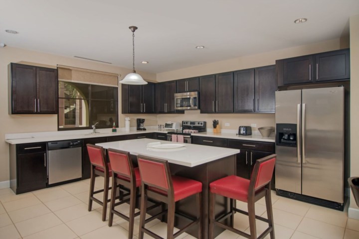 Modern kitchen with dark cabinets, stainless steel appliances, island with red chairs, and pendant light.