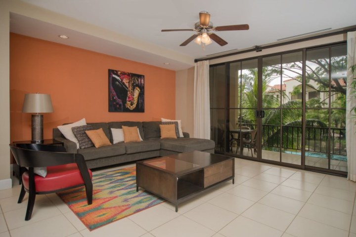 Living room with gray sofa, colorful rug, and glass doors opening to a balcony with greenery.