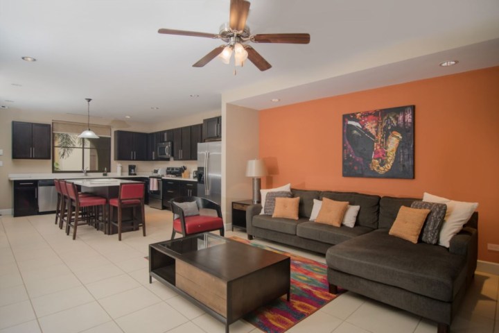 Open-plan living room and kitchen with brown furniture and orange accent wall.