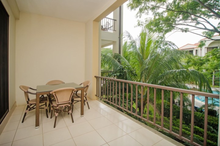 Outdoor balcony with table and chairs, overlooking lush greenery and palm trees.