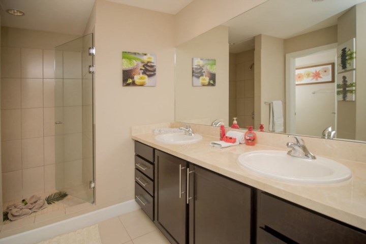 Bathroom with double sink, wall mirror, glass shower, and decorative artwork.