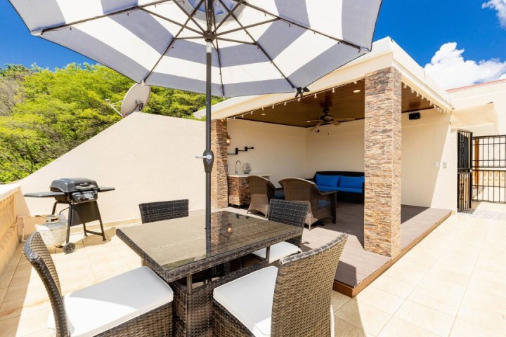Outdoor patio with wicker furniture, large umbrella, grill, and shaded seating area under a pergola.