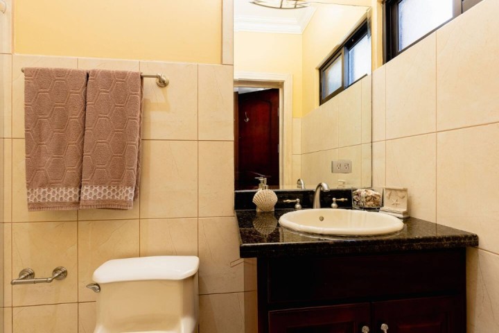 Bathroom with a sink, mirror, and towel on a rack. Beige tiles and dark counter.