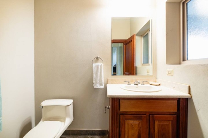 Bathroom with toilet, wall-mounted towel, sink with wooden cabinet, and a window.