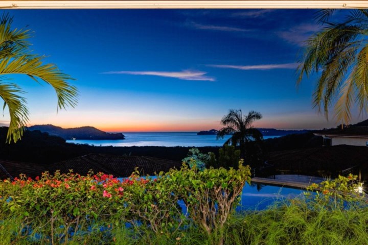 Tropical sunset view with palm trees, ocean, and colorful sky.