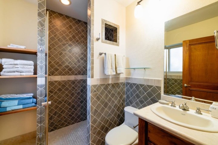 Modern bathroom with a glass shower, sink, toilet, and shelves with towels.