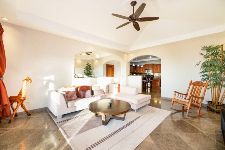 Spacious living room with white sectional, round table, rocking chair, and ceiling fan.