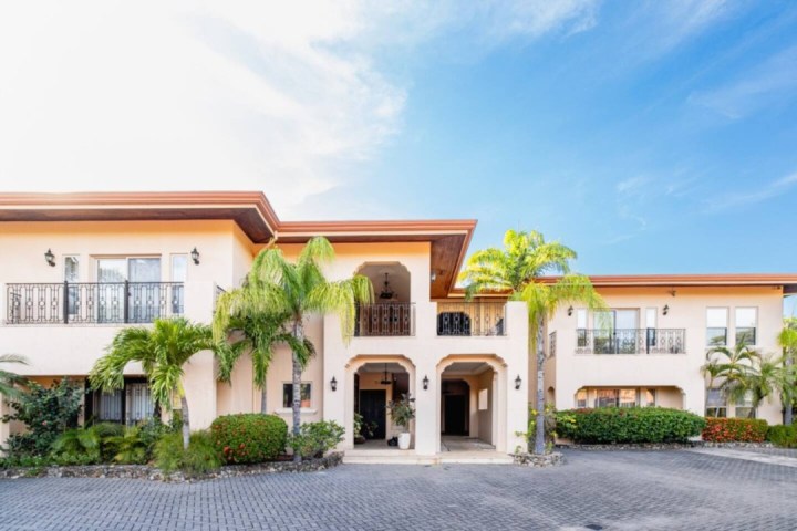 Two-story building with arches, balconies, and palm trees under a blue sky.