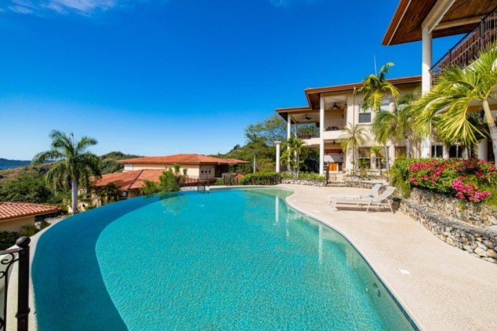 Luxury infinity pool at a villa with palm trees and blue sky background.