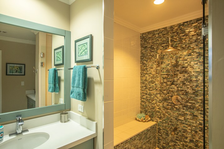 Bathroom with tiled shower, vanity with mirror, and blue towels hanging on the wall.