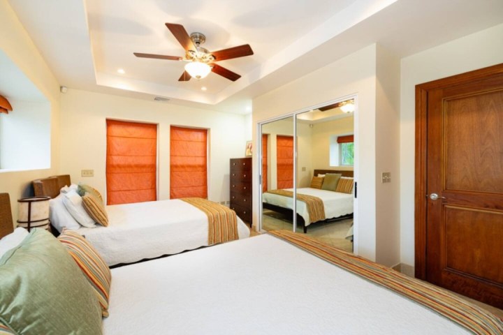 Bedroom with twin beds, mirrored closet, ceiling fan, and orange window shades.