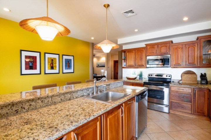 Modern kitchen with granite countertops, wooden cabinets, and yellow accent wall with framed art.