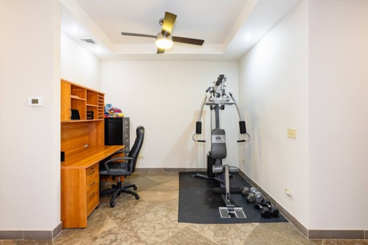 Room with desk, office chair, workout machine, and dumbbells on the floor.