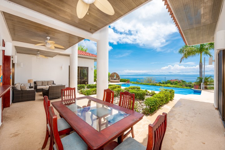 Outdoor patio with wooden dining table, pool, and ocean view.
