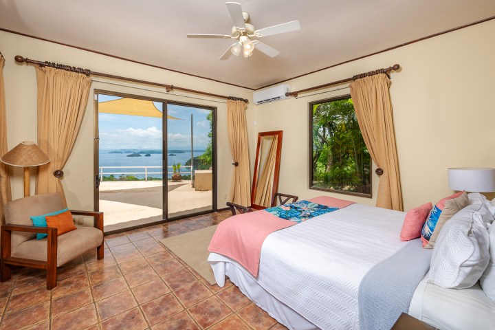 Spacious bedroom with ocean view, bed, armchair, and ceiling fan.