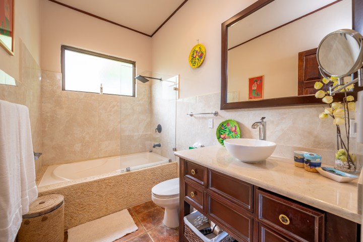 Modern bathroom with a bathtub, large mirror, and a white vessel sink on a wooden vanity.