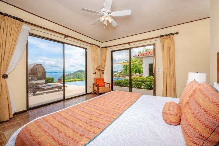 Bedroom with large windows showing ocean view and poolside patio.