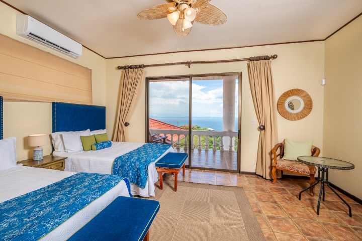 Bright bedroom with two beds, ocean view, and sliding doors to a balcony.