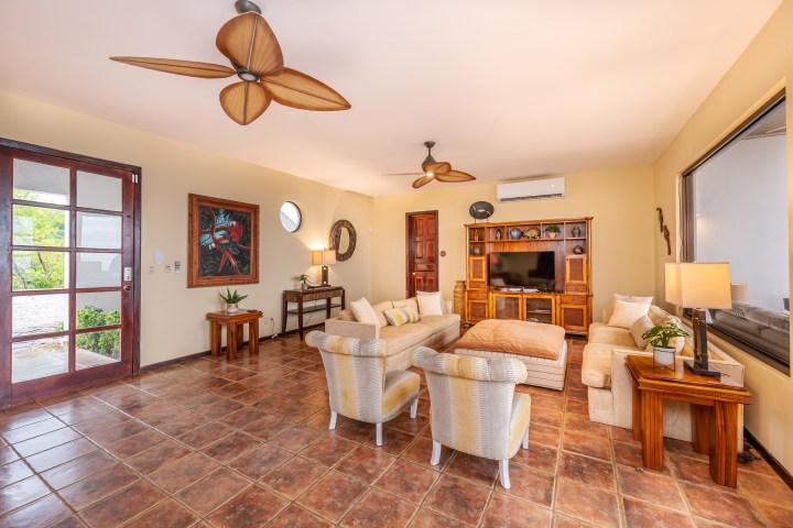 Spacious living room with beige furniture, brown floor tiles, and ceiling fans.