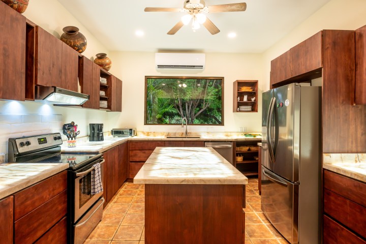 Modern kitchen with wooden cabinets, central island, stainless steel appliances, and window view.