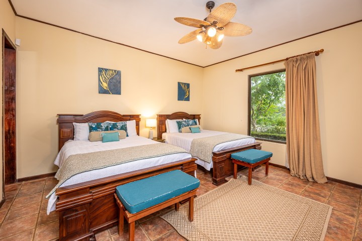 Bedroom with two beds, wooden furniture, ceiling fan, and a large window with curtains.