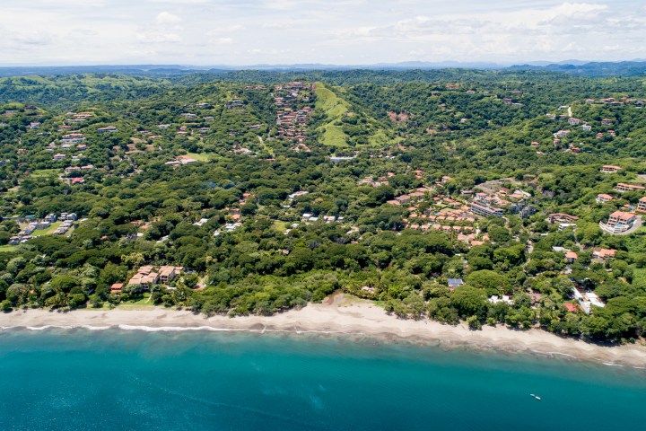 Aerial view of a coastal town with lush greenery, beach, and blue ocean.