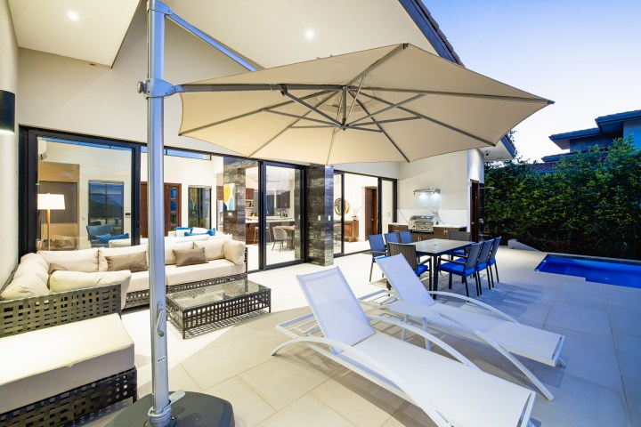 Modern patio with lounge chairs, dining set, large umbrella, and a pool in a spacious outdoor area.