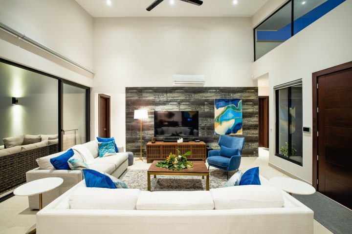 Modern living room with white sofas, blue armchair, and TV on wood accent wall.