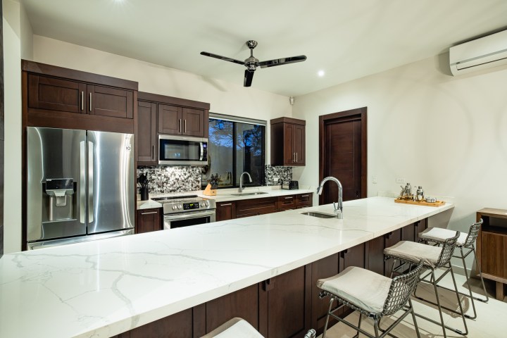 Modern kitchen with dark wood cabinets, white island countertop, and stainless steel appliances.