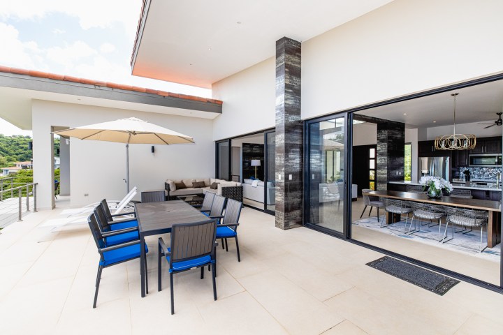 Modern outdoor patio with dining set, umbrella, and view into sleek kitchen and living room.