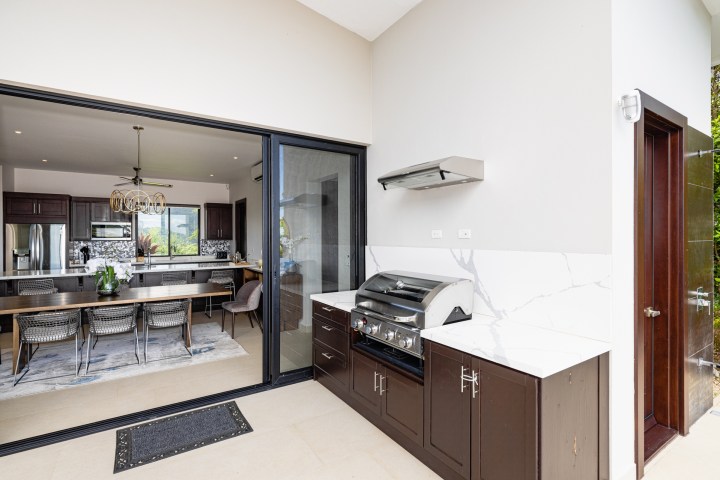 Open kitchen and dining area with outdoor grill on patio, modern decor.
