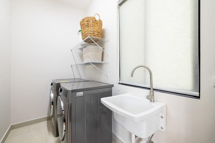Laundry room with washer, dryer, shelves, and sink under a window shade.