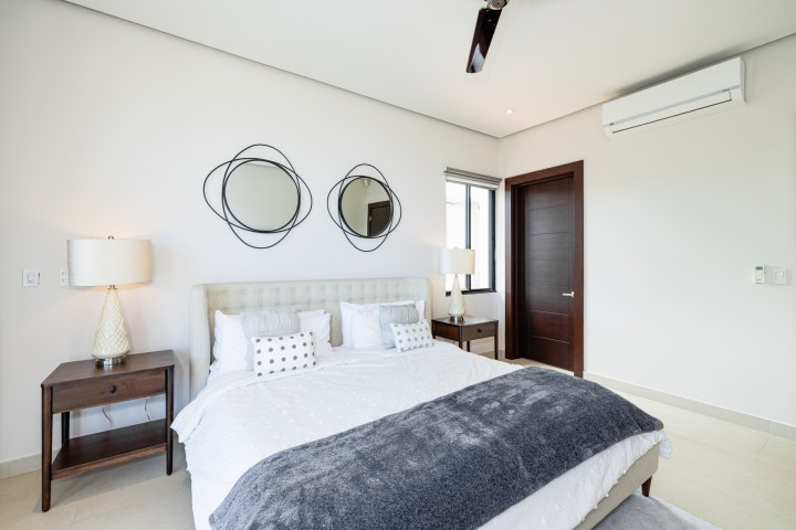 Modern bedroom with bed, two nightstands, lamps, mirrors, and an air conditioner.
