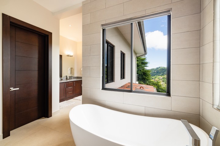 Modern bathroom with freestanding tub and large window with mountain view.