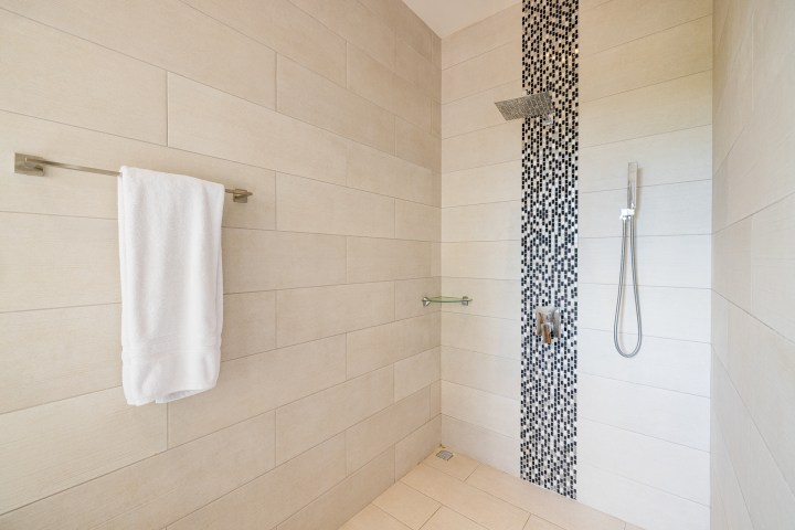 Modern shower with beige tiles, black mosaic strip, and wall-mounted towel and handheld showerhead.