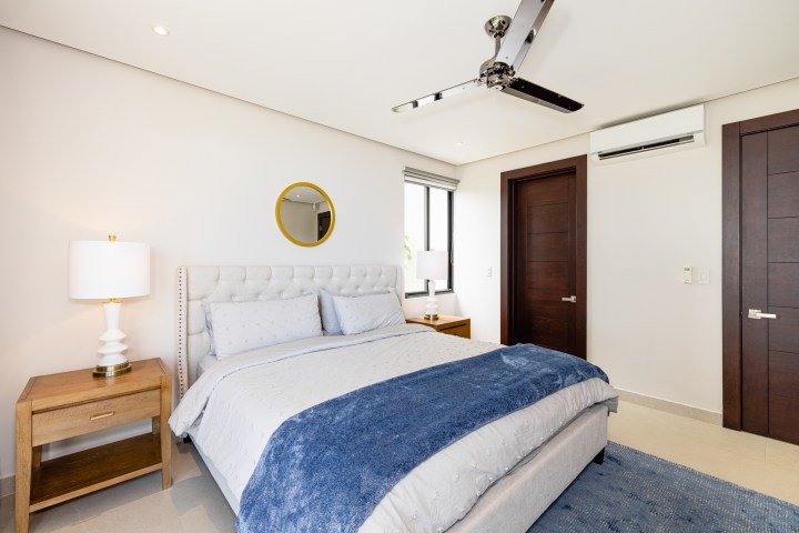 Modern bedroom with a gray bed, blue blanket, two wooden nightstands, a ceiling fan, and a window.