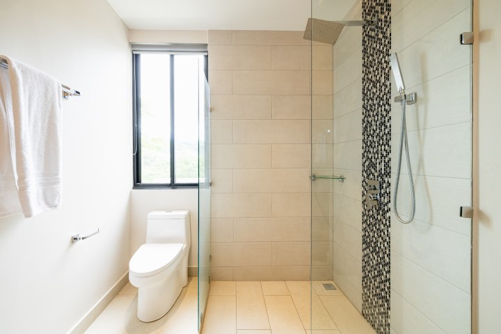 Modern bathroom with toilet, shower, and a towel rack beside a window.